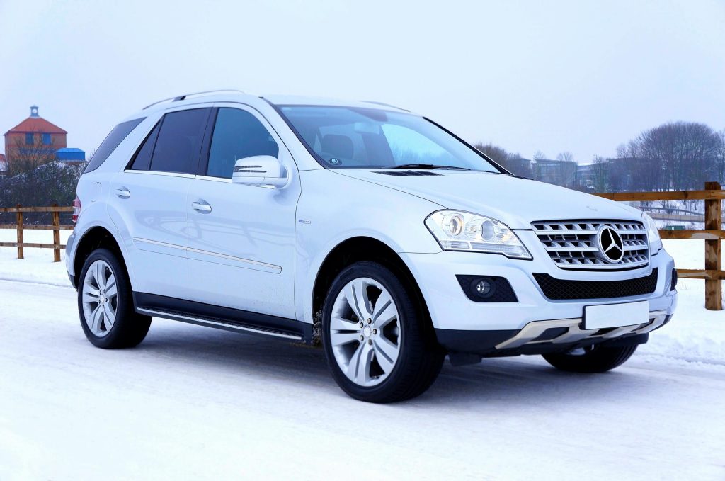 Luxurious white SUV navigating snowy road in winter with scenic background in Scotland.
