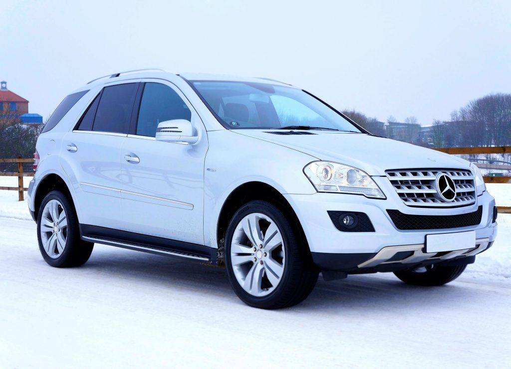 Luxurious white SUV navigating snowy road in winter with scenic background in Scotland.