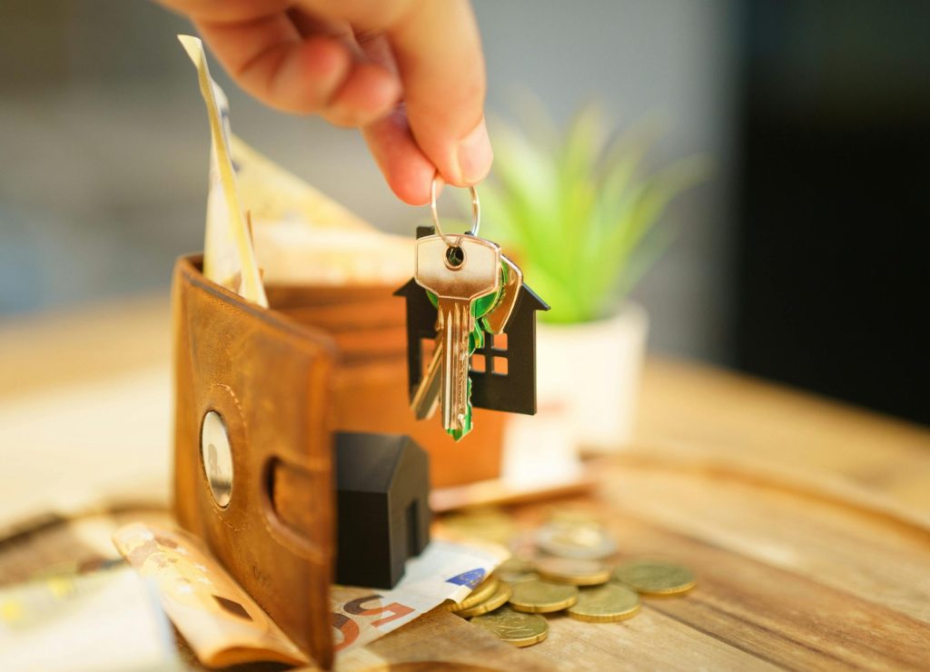 Close-up of hand holding a house key with a wallet and coins, symbolizing real estate investment.